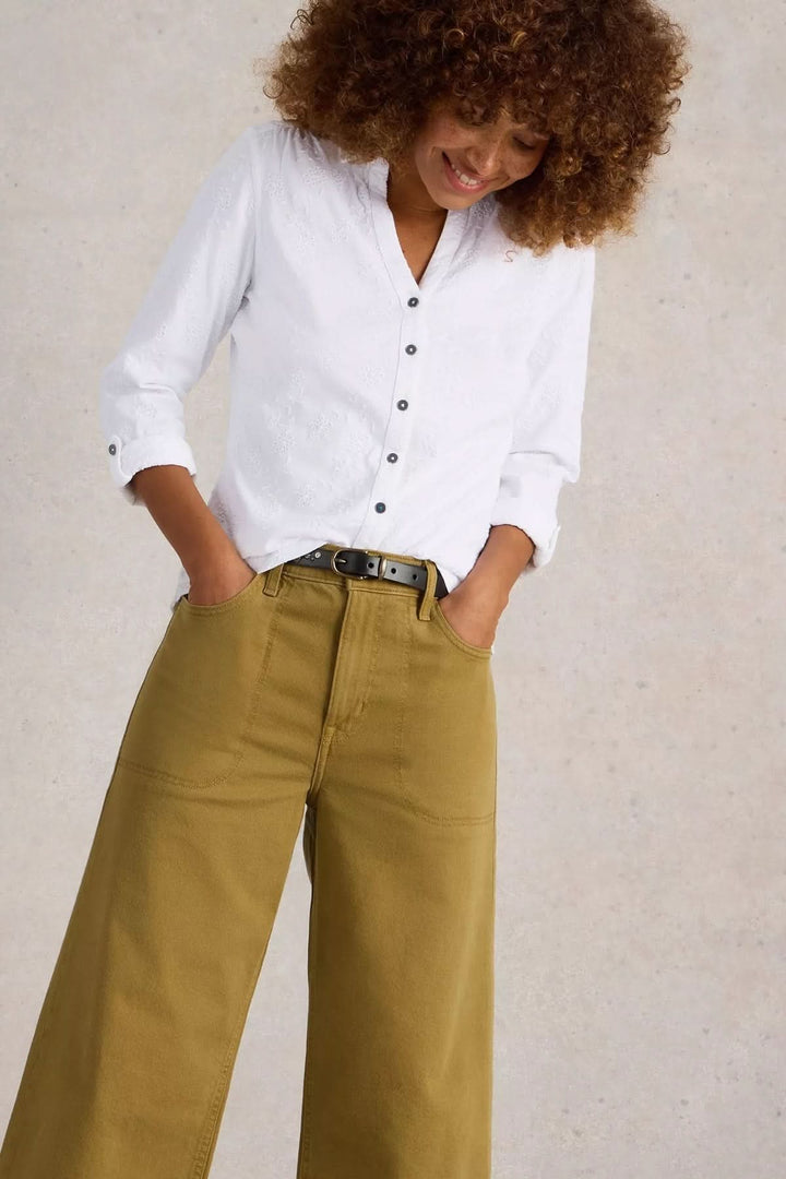 Femme souriante portant une chemise blanche et un pantalon large, style décontracté et élégant.