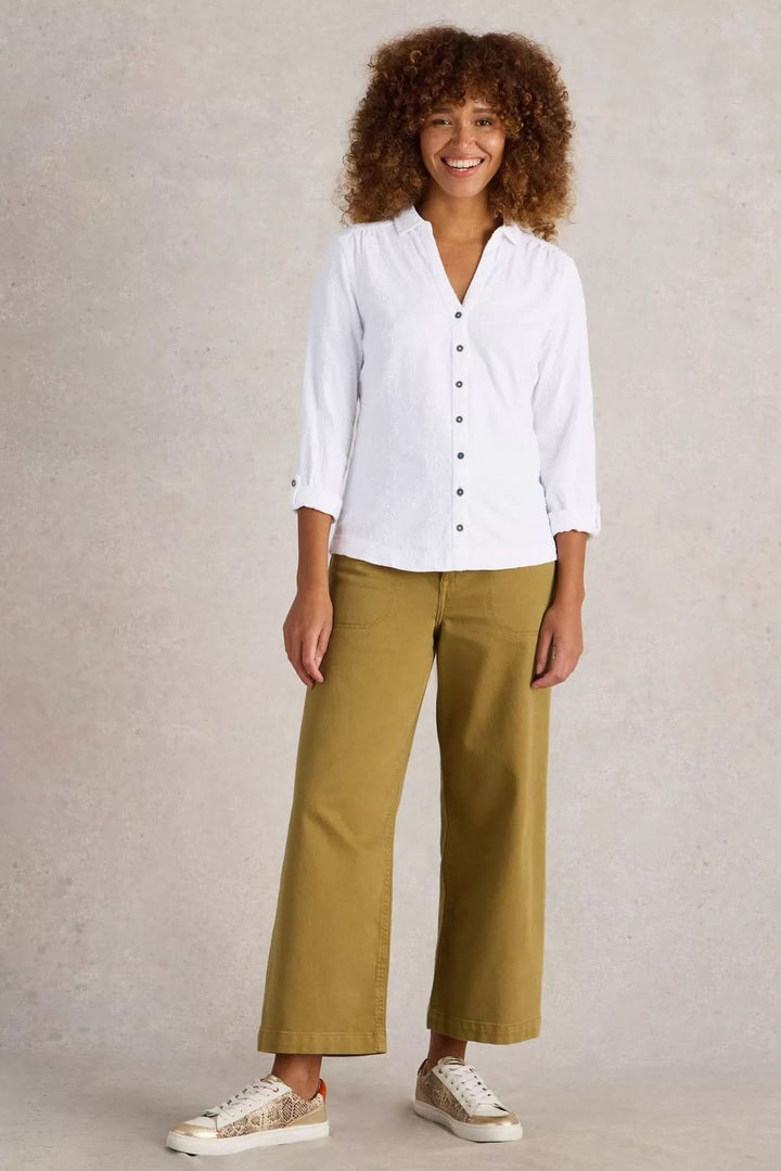 Femme souriante portant une chemise blanche à broderie et un pantalon olive, idéal pour un look décontracté et élégant.