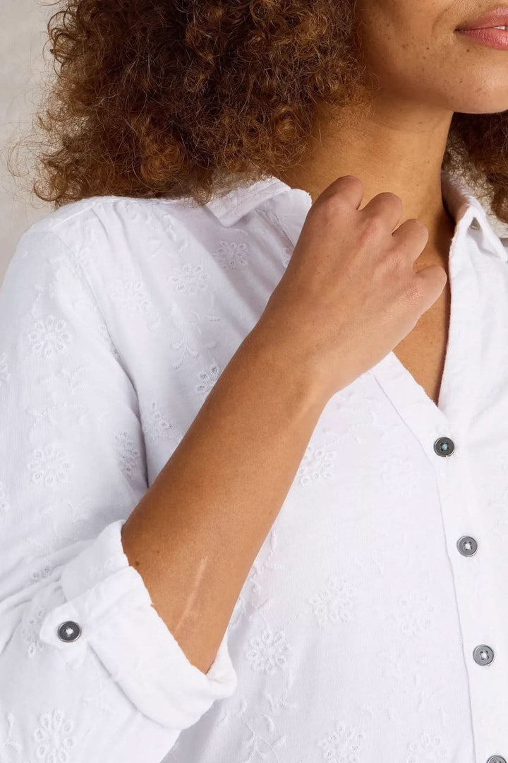 Femme portant une chemise blanche en coton avec broderie délicate et encolure en V, détails de boutons en métal.