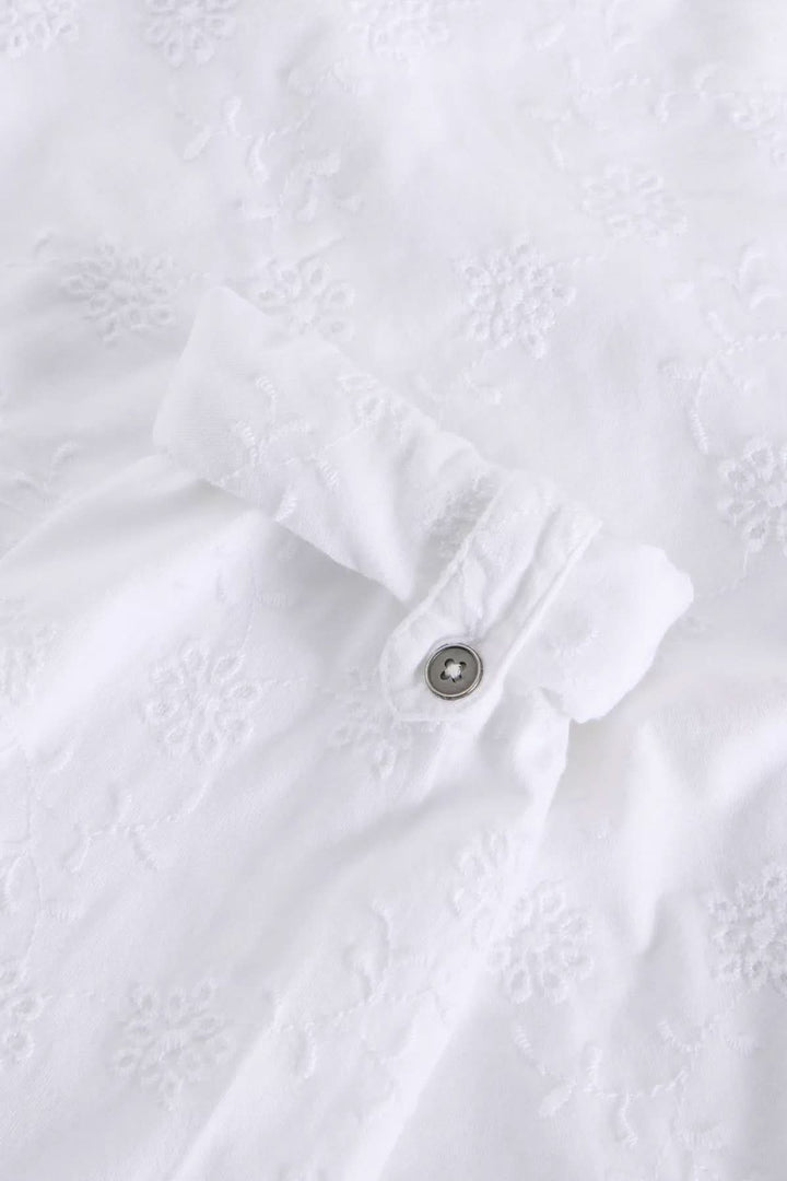 Chemise blanche en coton avec broderie subtile et détail de bouton sur la manche, élégante et confortable.