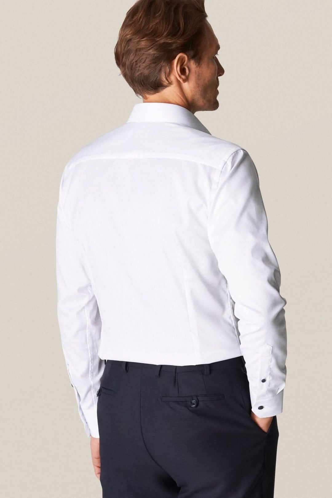 Homme portant une chemise blanche élégante avec boutons contrastés, vue de dos, style business.