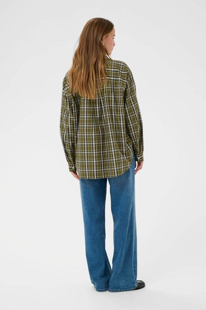 Femme portant une chemise à carreaux verte et un jean, vue de dos, illustrant un style casual chic et décontracté.