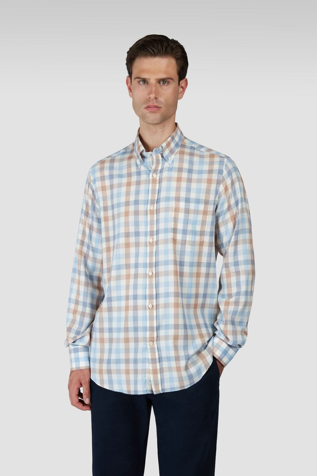 Homme portant une chemise à carreaux manches longues col boutonné, tenue moderne et polyvalente avec motif classique.