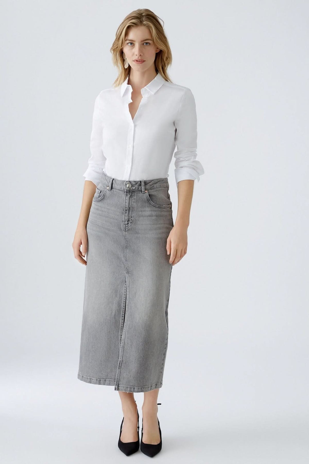 Femme portant une chemise blanche classique et une jupe longue en jean gris, style chic décontracté.