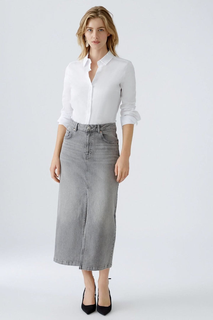 Femme portant une chemise blanche classique et une jupe longue en jean gris, style chic décontracté.