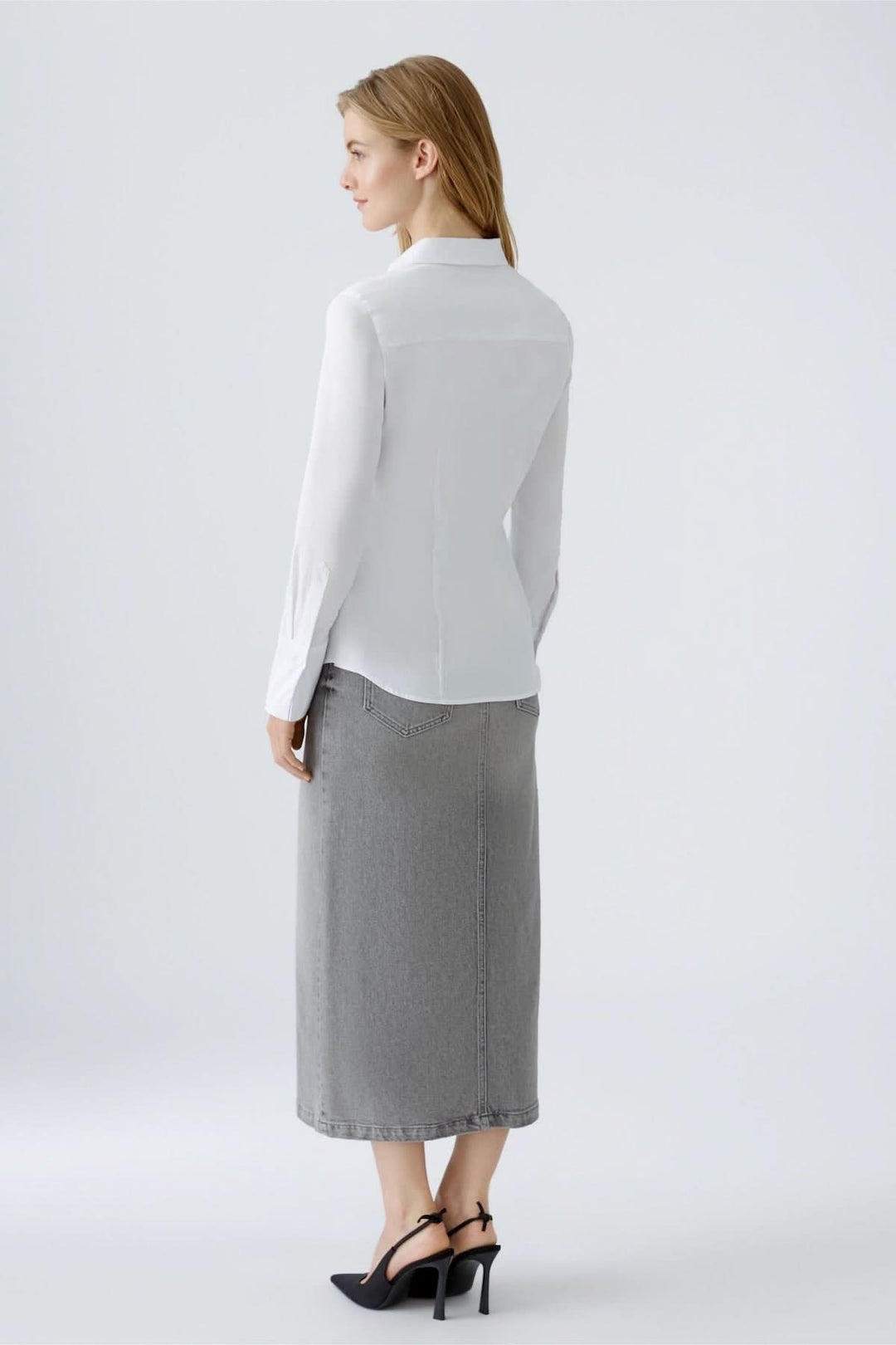 Femme portant une chemise blanche ajustée avec une jupe grise, vue de dos dans un cadre épuré.