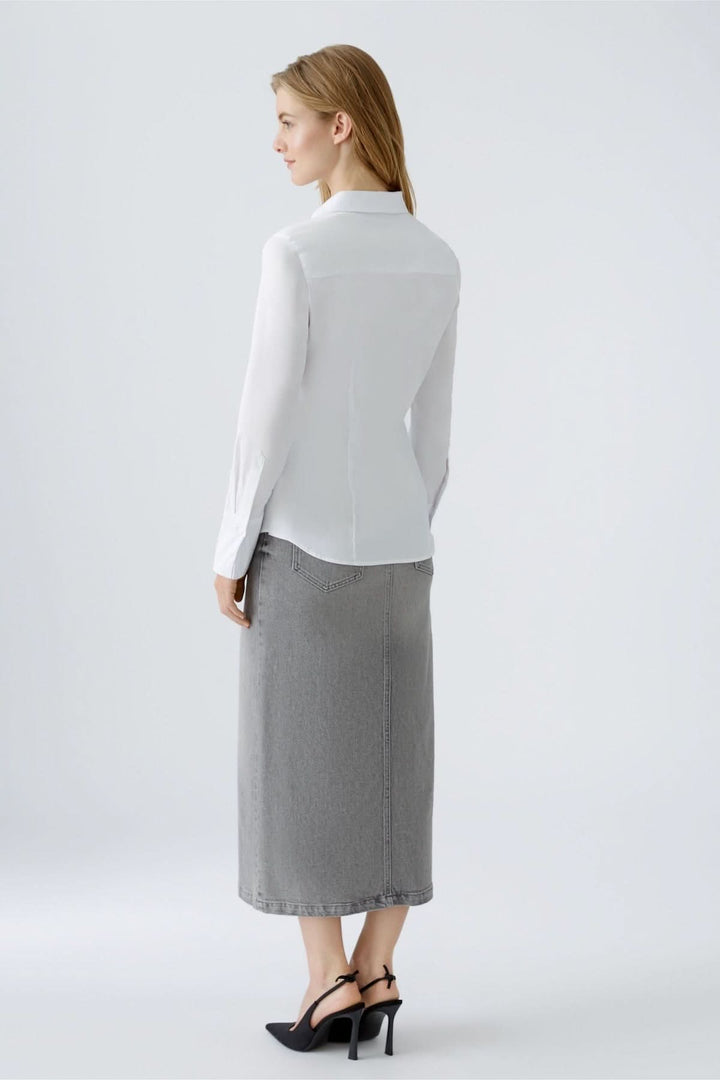 Femme portant une chemise blanche ajustée avec une jupe grise, vue de dos dans un cadre épuré.