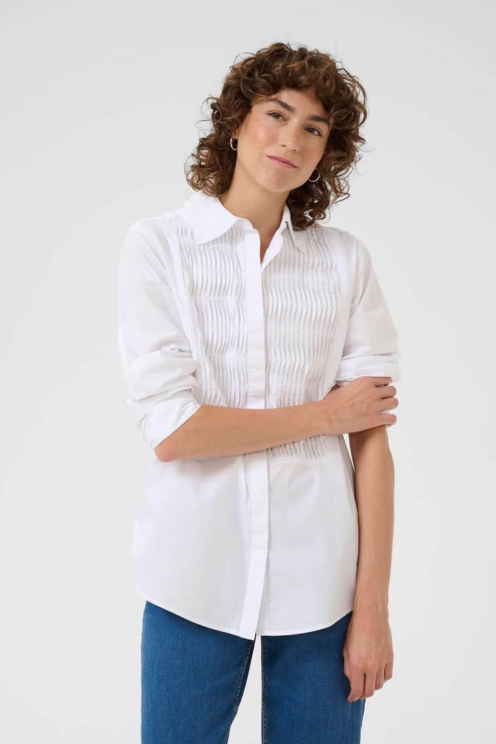 Femme portant une chemise classique blanche avec plis nervurés, coupe droite, col chemise, associée à un jean décontracté.