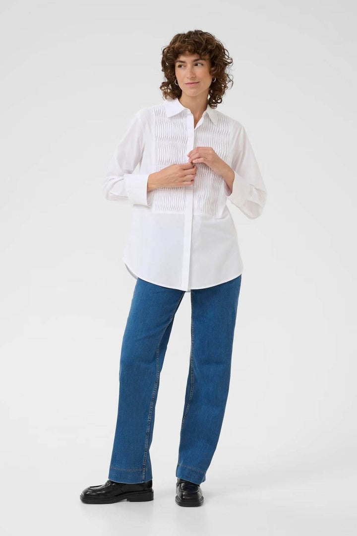 Femme portant une chemise classique blanche avec plis nervurés, coupe droite, col chemise, associée à un jean pour un look décontracté.