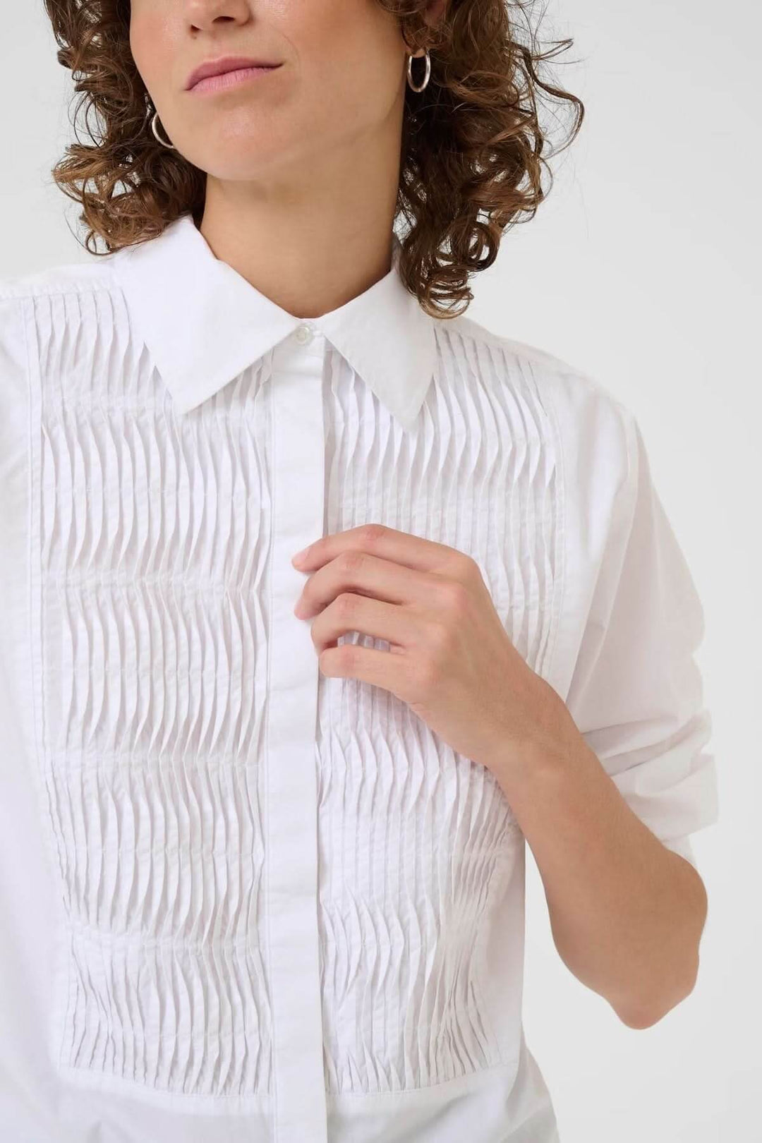 Femme portant une chemise blanche classique avec plis nervurés, col chemise et coupe droite, style élégant et polyvalent.