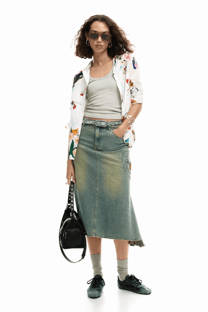 Femme portant une chemise collage fleurs avec imprimé artistique et jupe en jean, accessoirisée de lunettes de soleil et sac noir.