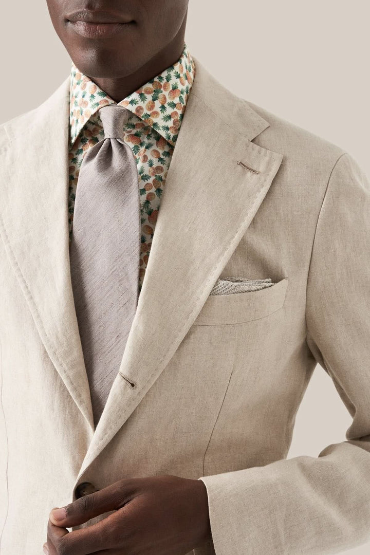Homme portant un costume en lin avec chemise à motifs floraux et cravate grise, style élégant.