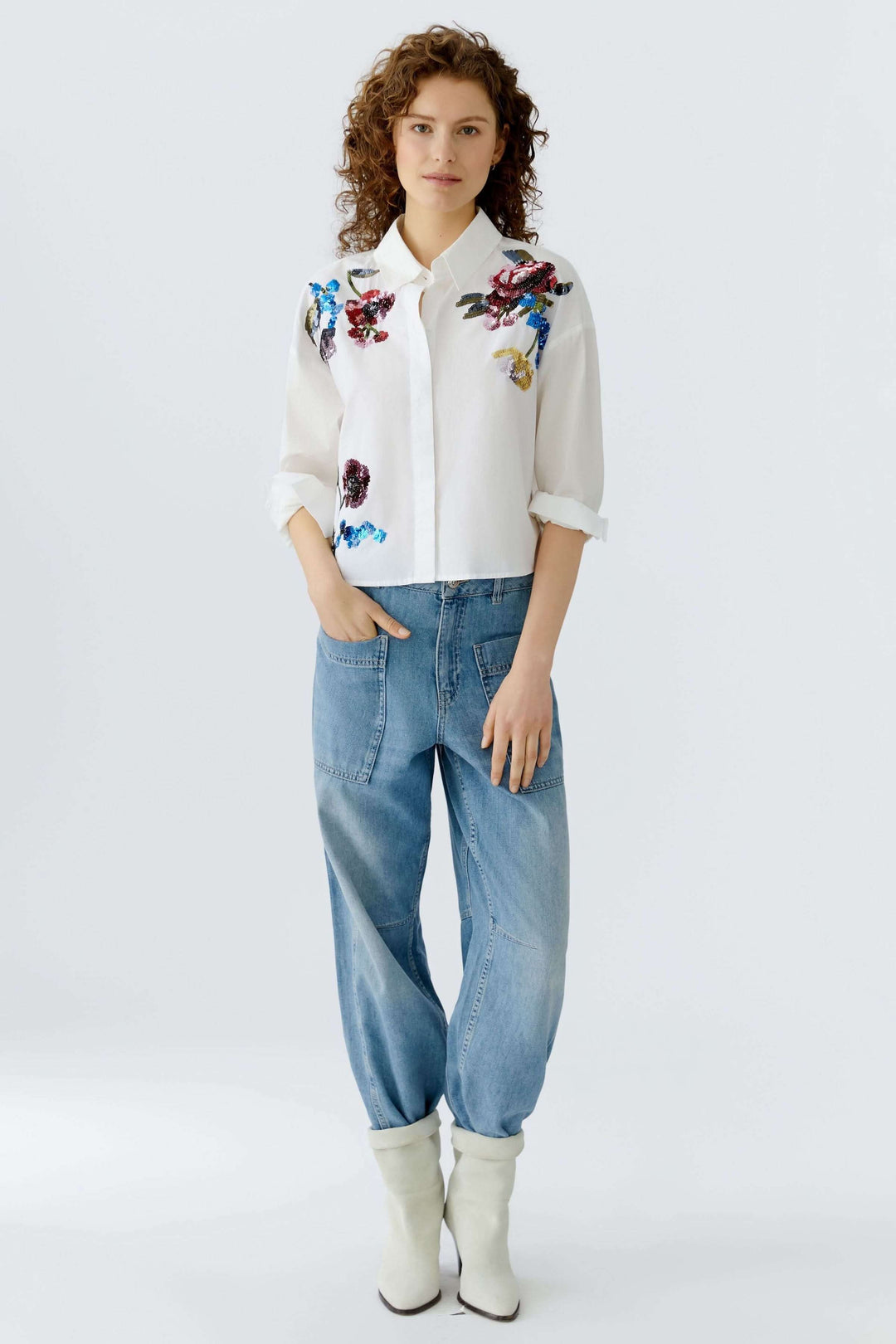 Chemise coupe moderne avec broderies florales, portée avec un jean décontracté et des bottes blanches.