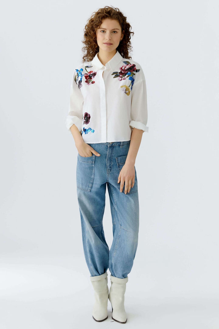 Chemise coupe moderne avec broderies florales, portée avec un jean décontracté et des bottes blanches.