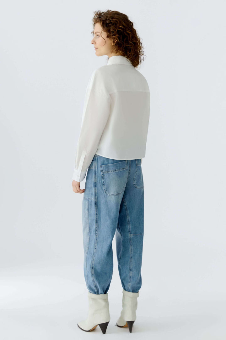 Femme portant une chemise coupe moderne avec broderies florales, vue arrière avec un jean ample et des bottes blanches.