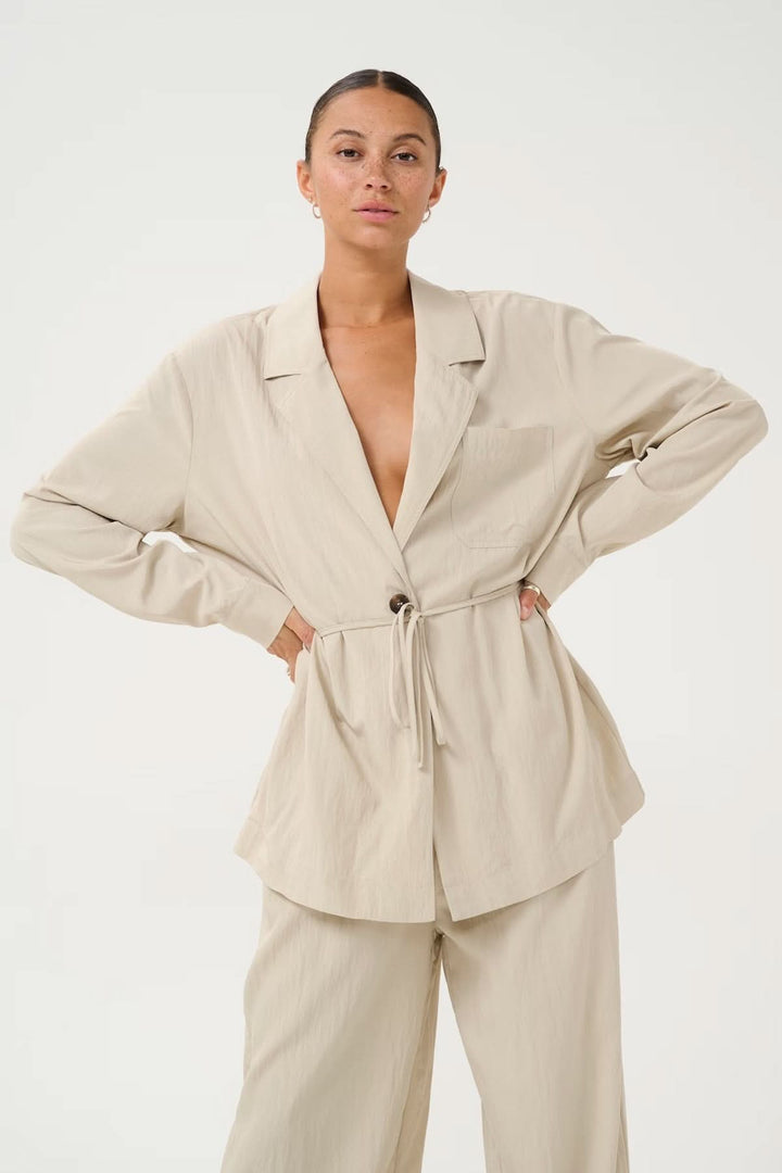 Chemise décontractée beige avec col à revers et ceinture ajustable, idéale pour un look élégant et confortable.