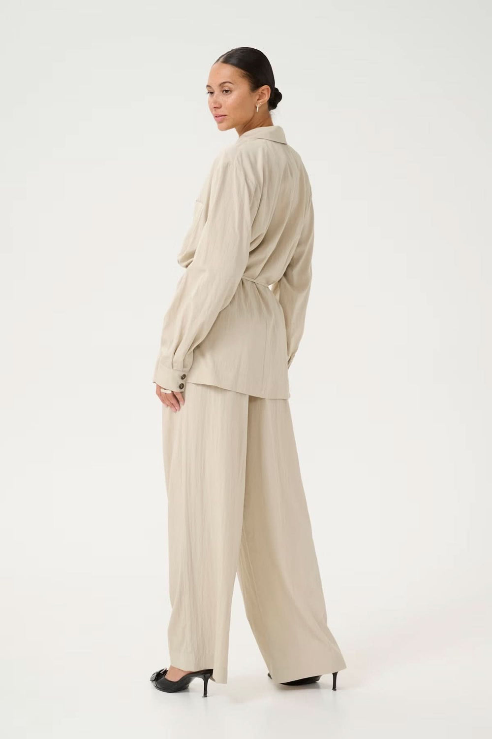Femme portant un blazer fluide beige avec une coupe décontractée, vue de dos en pantalon large.
