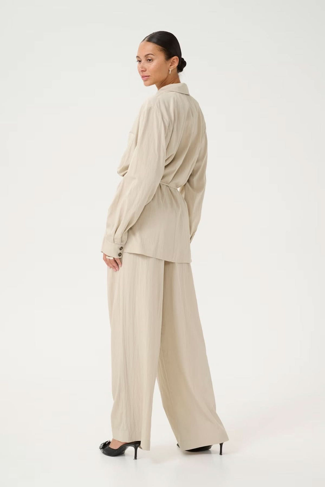 Femme portant un blazer fluide beige avec une coupe décontractée, vue de dos en pantalon large.