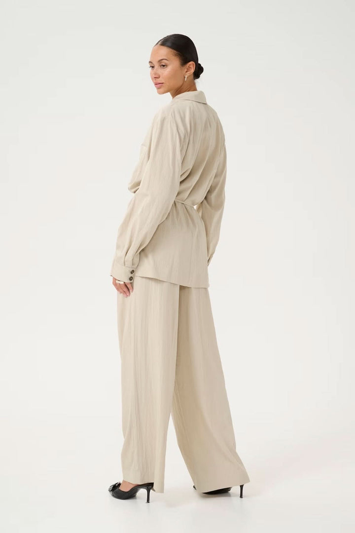 Femme portant un blazer fluide beige avec une coupe décontractée, vue de dos en pantalon large.