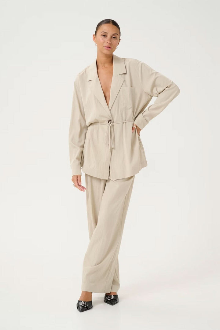 Blazer fluide à coupe décontractée avec ceinture ajustable, combiné avec un pantalon assorti dans des tons beiges.