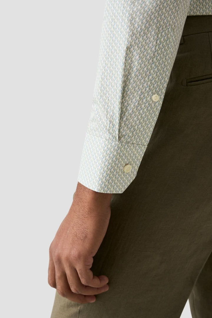 Chemise en coton à imprimé perroquet, détails élégants en vert et bleu, portée avec un pantalon stylé.