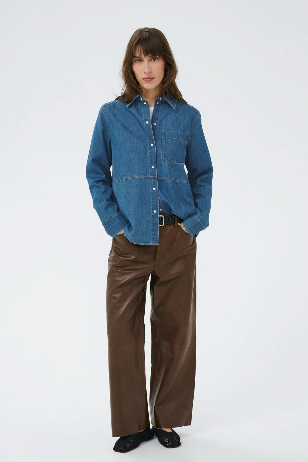 Femme portant la chemise en denim Alvine avec surpiqûres apparentes, sobre et versatile, correspond au look quotidien. Décris moi le produit en français.