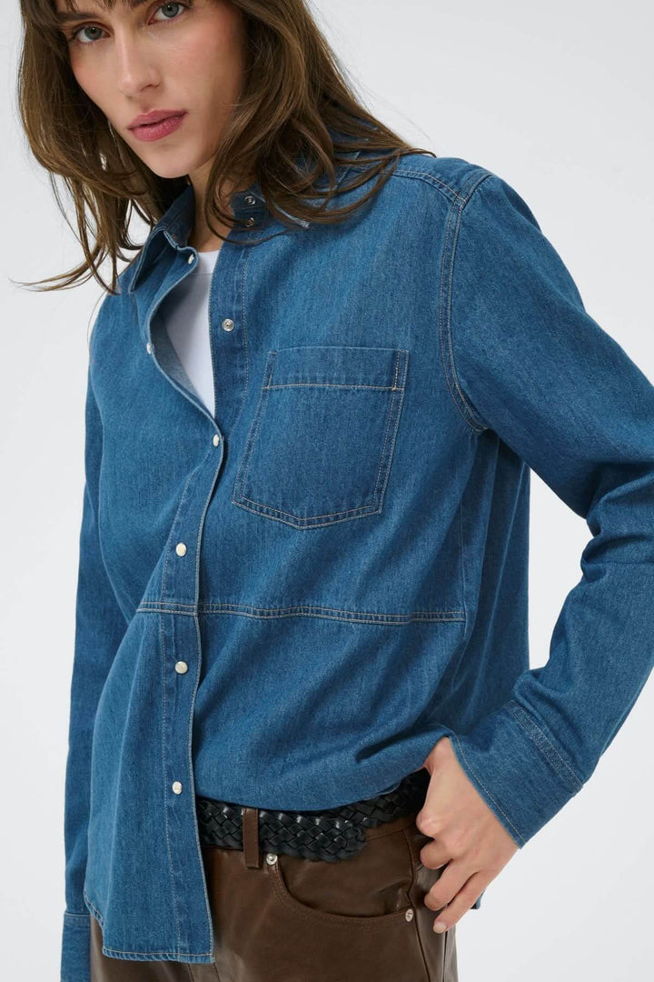 Chemise en denim Alvine avec poche poitrine et surpiqûres apparentes, portée ouverte pour un look décontracté et structuré.