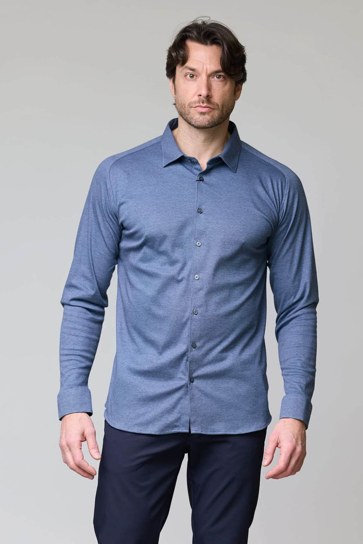 Homme portant une chemise en jersey extensible bleue à manches longues, coupe ajustée, col structuré. Chemise moderne et polyvalente.