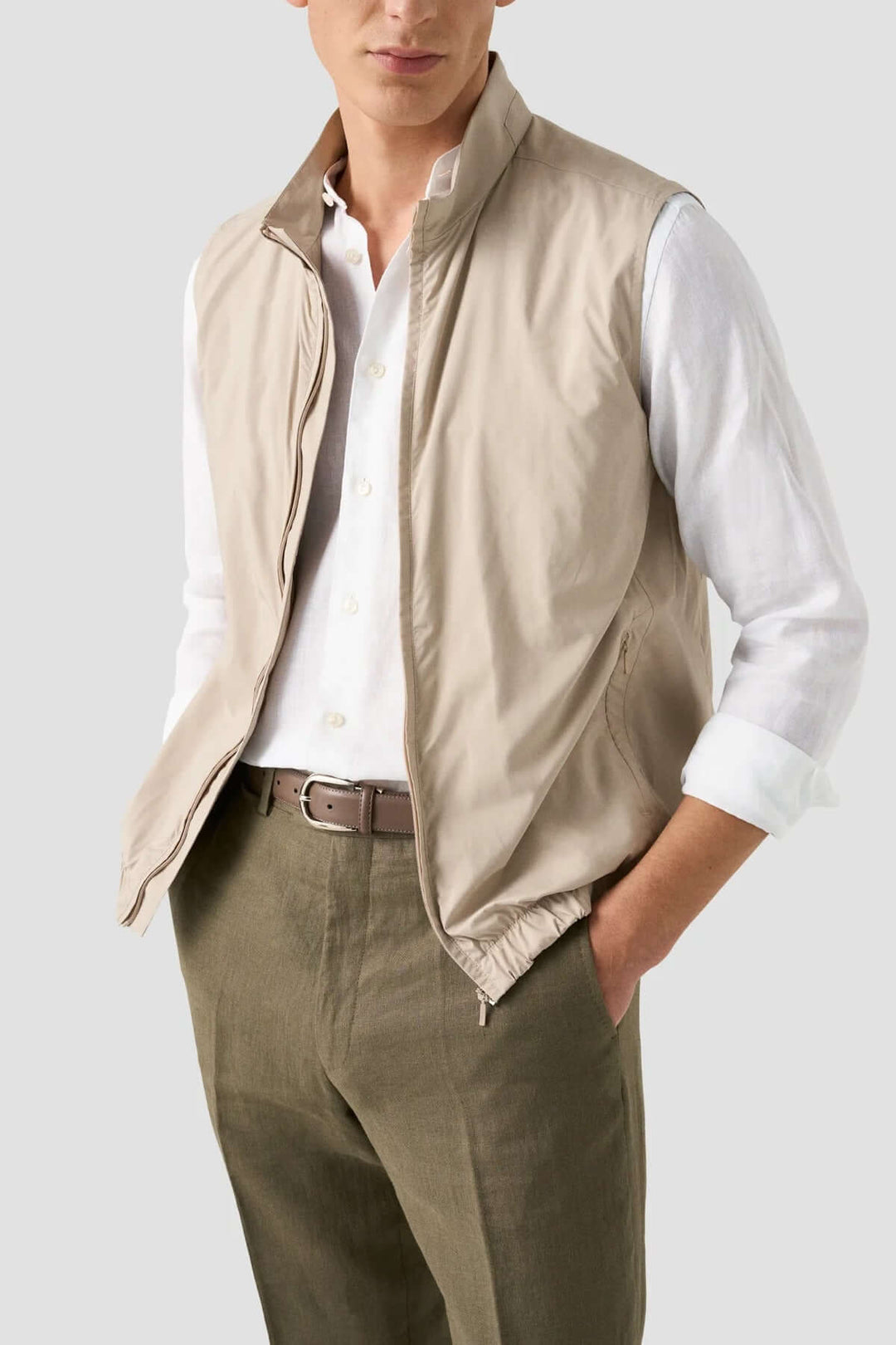 Homme portant un gilet beige léger sur une chemise blanche et un pantalon olive, style décontracté et élégant.