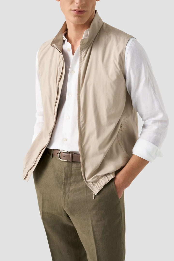 Homme portant un gilet beige léger sur une chemise blanche et un pantalon olive, style décontracté et élégant.