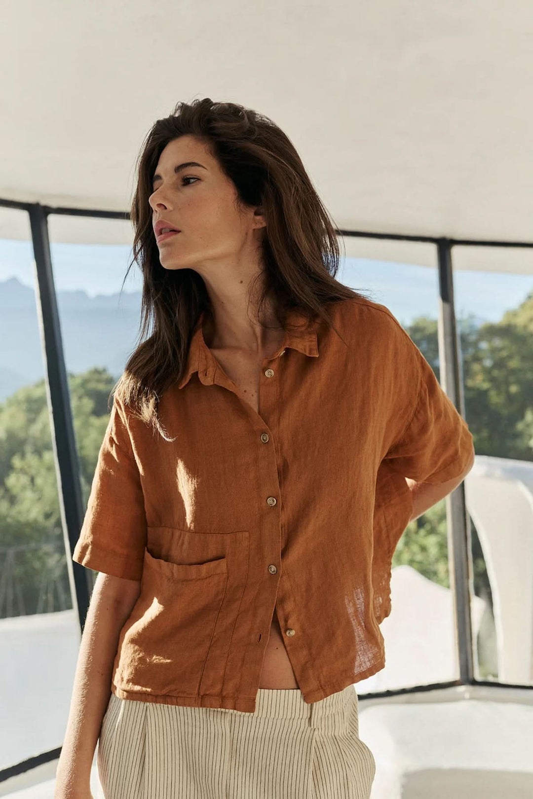 Femme portant une chemise en lin à coupe décontractée, couleur marron, avec col classique et poche, dans un cadre estival.