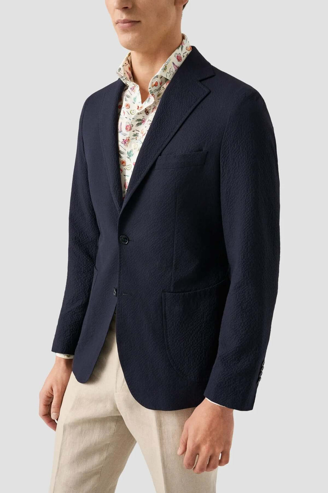 Veste en bleu marine portée sur une chemise à motifs floraux, parfaite pour un look estival élégant.