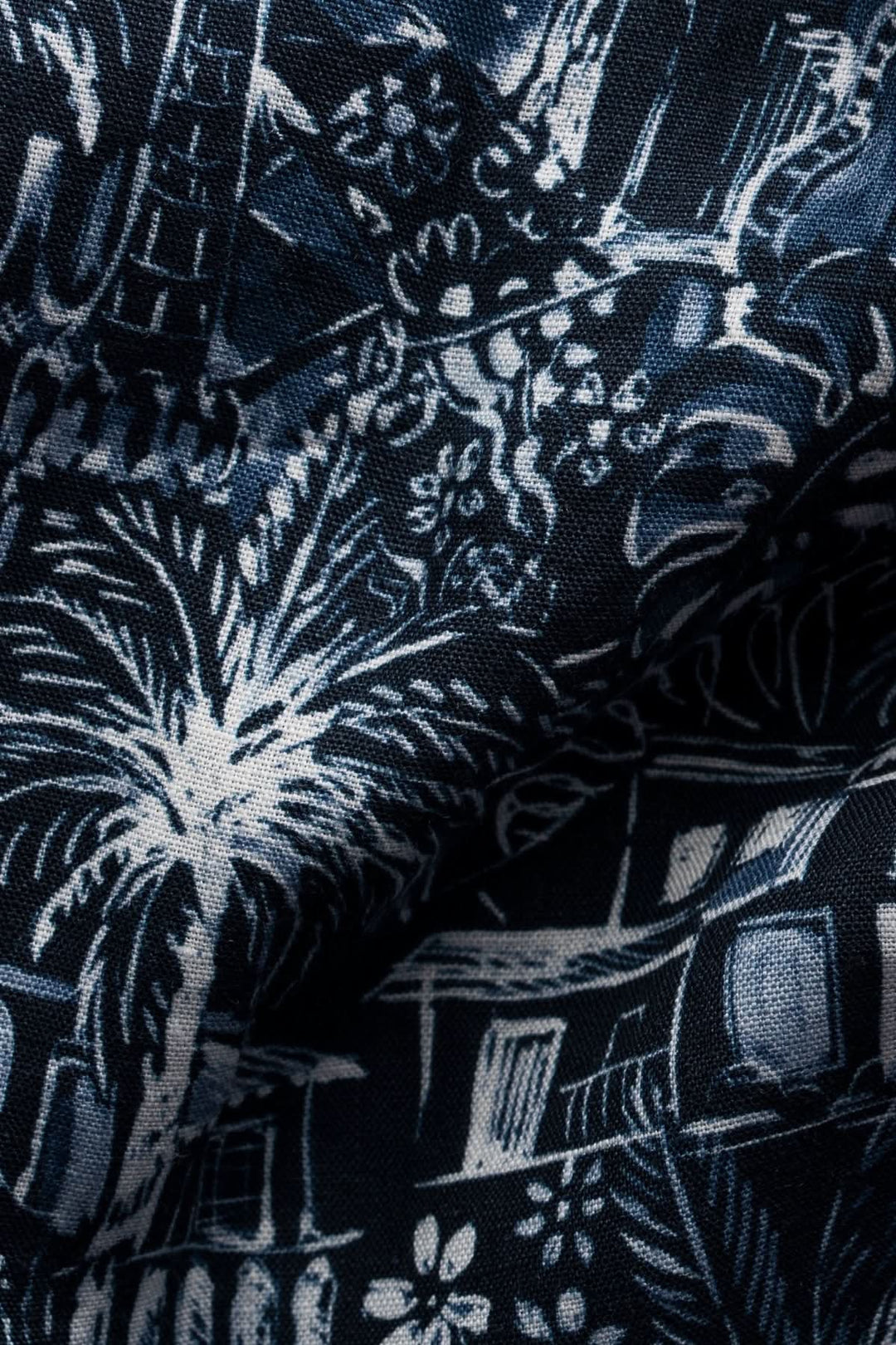 Imprimé tropical détaillé en bleu et blanc sur tissu en lin, évoquant des paysages exotiques et estivaux.