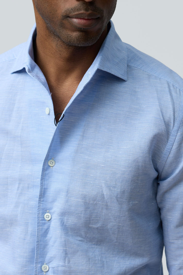 Chemise en lin légère et raffinée portée par un homme, coupe ajustée, col classique et boutons sur le devant, couleur bleu clair.