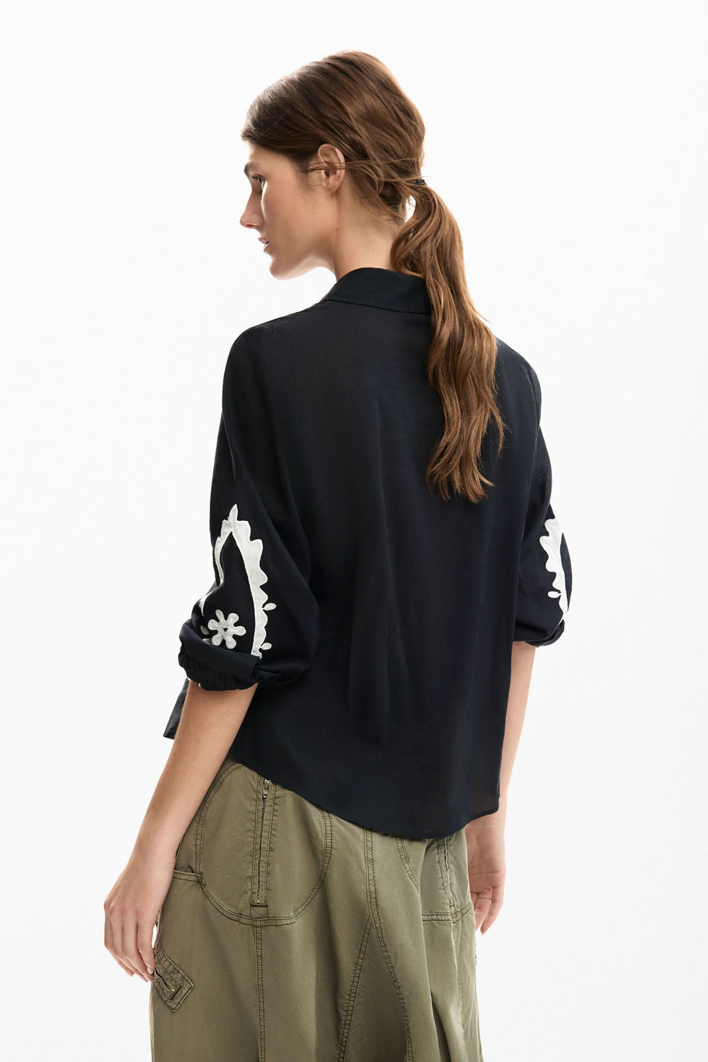Dos d'une femme portant une chemise fluide à broderies contrastées avec manches retroussées, style élégant et décontracté.