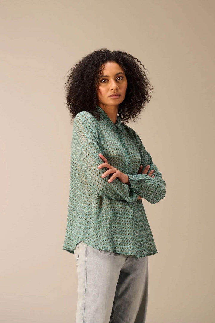 Femme portant une chemise fluide imprimé avec un motif géométrique, manches longues, et col classique, associée à un jean.