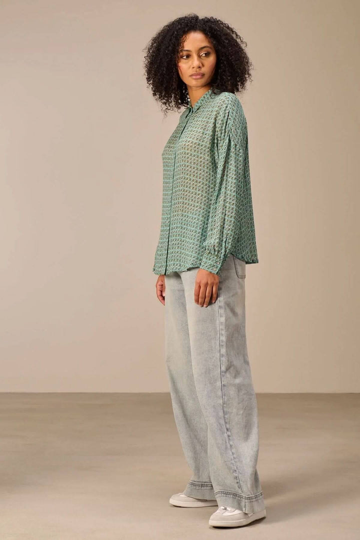 Chemise fluide imprimé à motifs géométriques raffinés, coupe décontractée, col classique et patte de boutonnage, portée avec un jean.