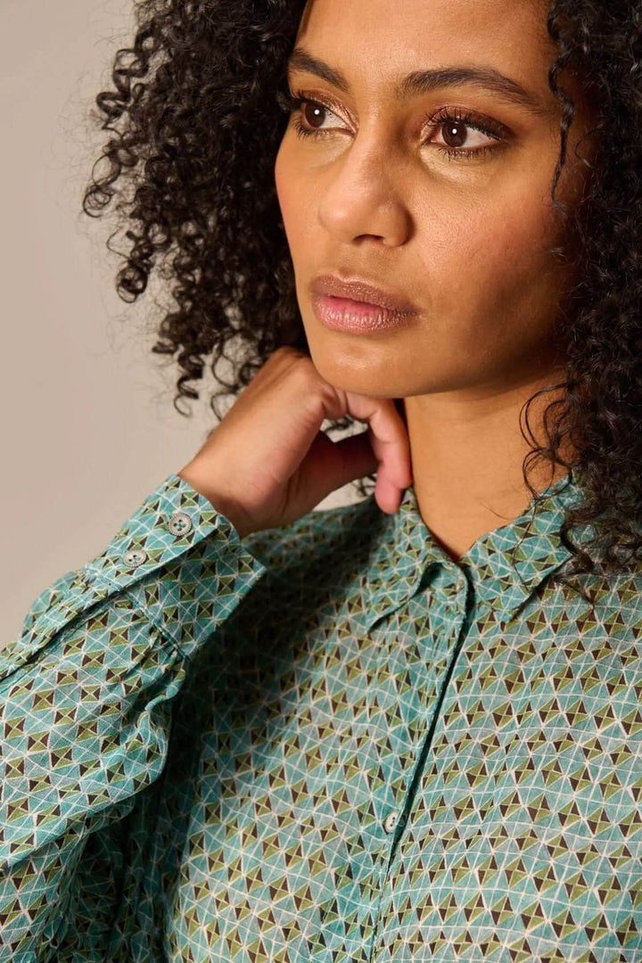 Femme portant une chemise fluide imprimé avec un motif géométrique raffiné et un col classique, style moderne et confortable.