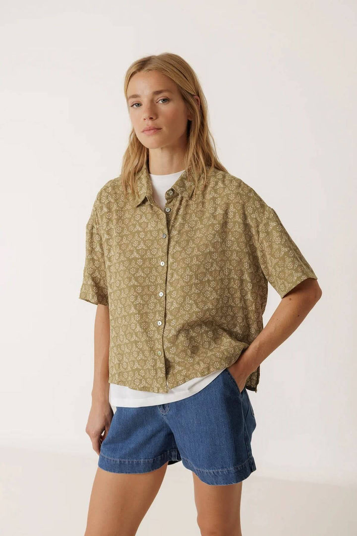 Femme portant une chemise fluide imprimée à manches courtes, style décontracté, col classique, sur fond neutre.