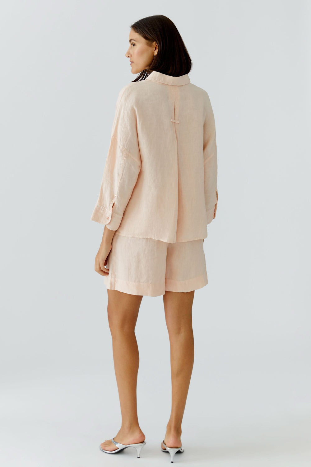 Vue arrière d'une tenue décontractée beige avec chemise fluide à manches longues et short assorti.
