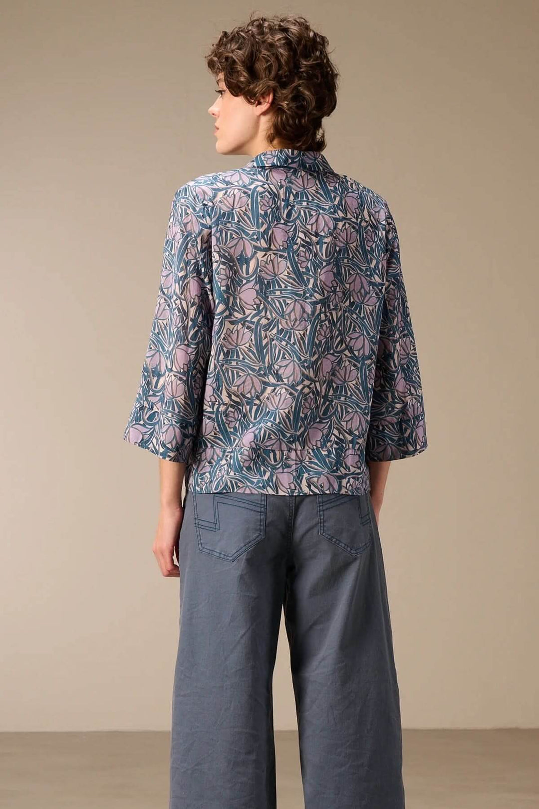 Modèle portant une chemise fluide à manches trois-quarts avec imprimé, vue de dos, montré avec un pantalon large bleu.