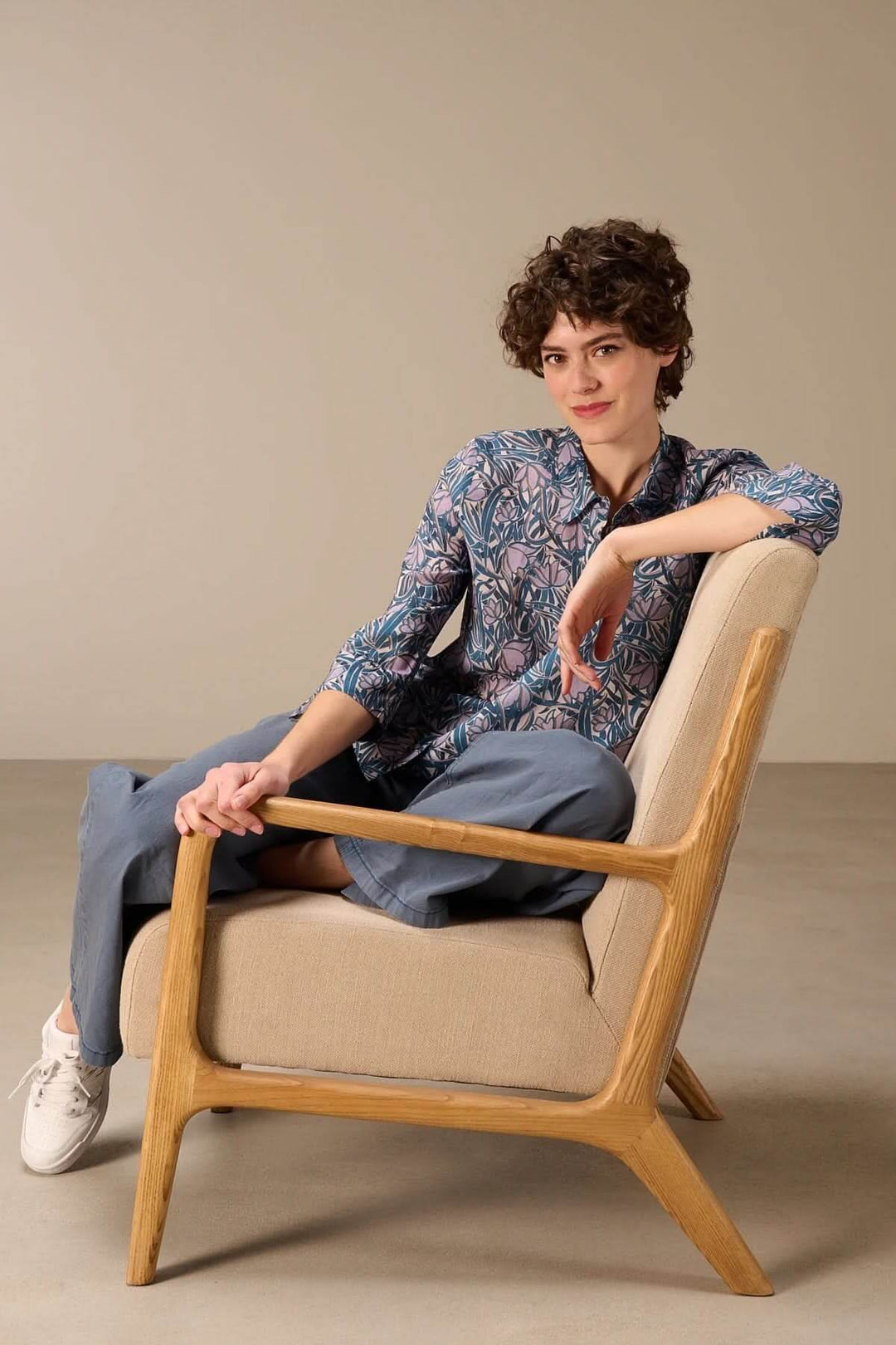 Femme portant une chemise fluide à manches trois-quarts avec imprimé, assise dans un fauteuil, style élégant et décontracté.