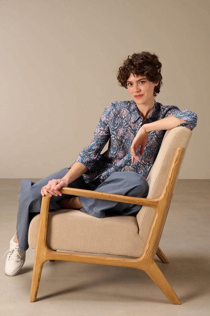 Femme portant une chemise fluide à manches trois-quarts avec imprimé, assise dans un fauteuil, style élégant et décontracté.