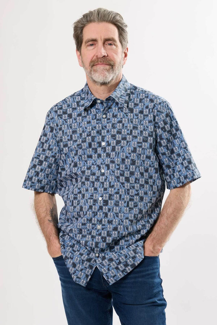 Chemise à manches courtes avec imprimé graphique aux tons bleus et motifs stylisés, portée par un homme.