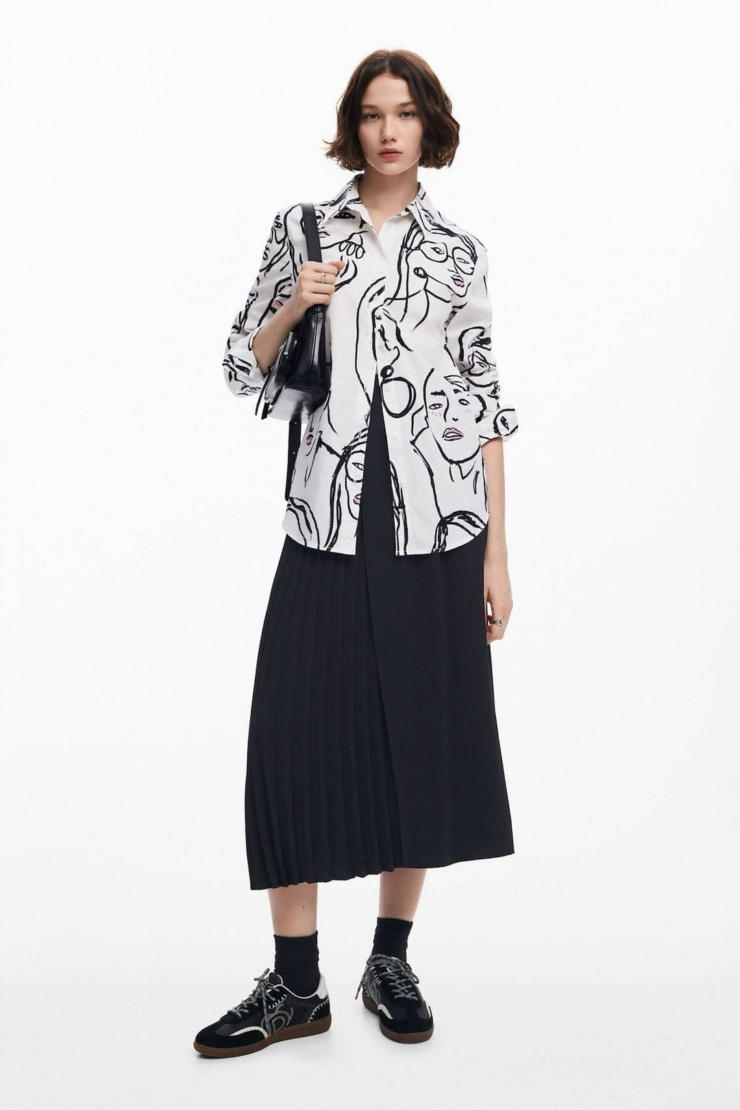 Chemise à imprimé artistique de visages féminins, portée avec une jupe plissée pour un look chic et moderne.