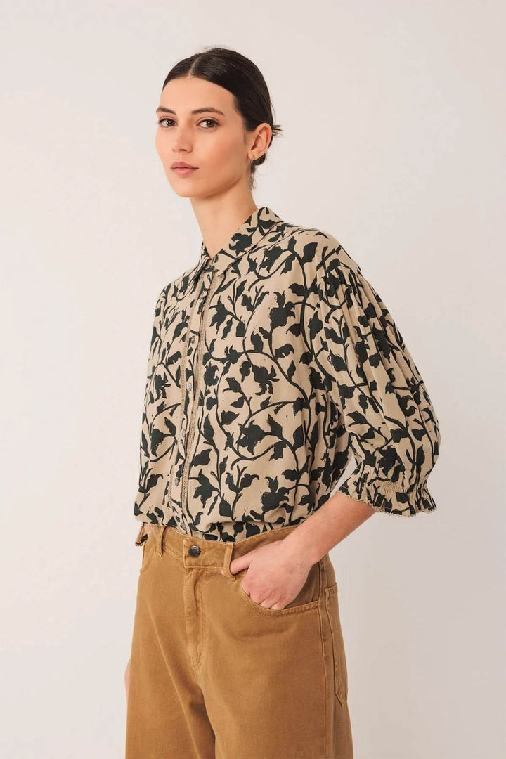 Chemise imprimée à la coupe fluide avec motif végétal, col chemise classique et manches bouffantes, portée avec un pantalon marron.