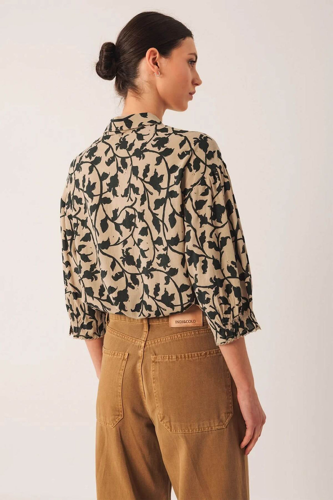 Femme portant une chemise imprimée à motif végétal avec col classique, manches bouffantes et coupe fluide, style élégant.