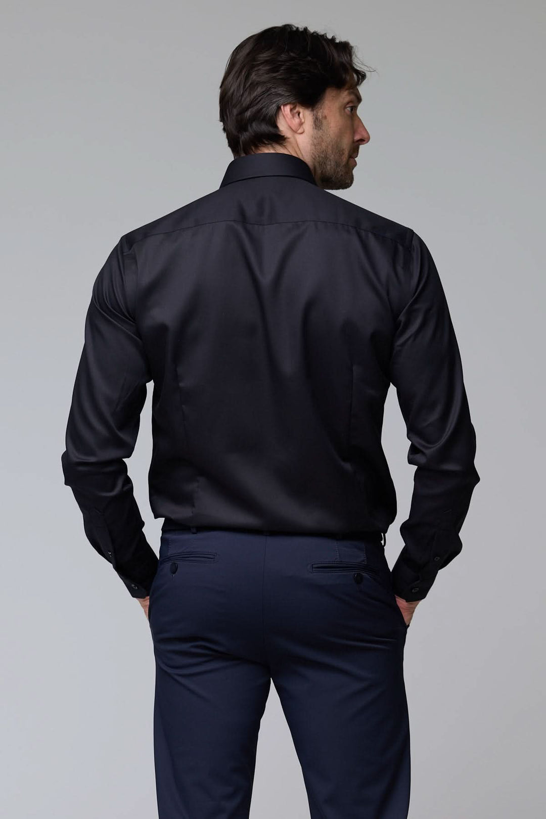 Homme portant une chemise habillée satinée noire à manches longues, accentuant l'élégance et la modernité.