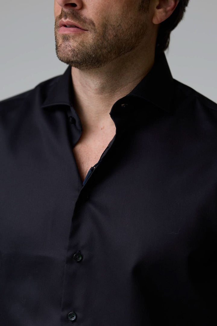 Homme portant une chemise habillée satinée noire avec col ouvert et manches longues, idéale pour un look élégant et moderne.