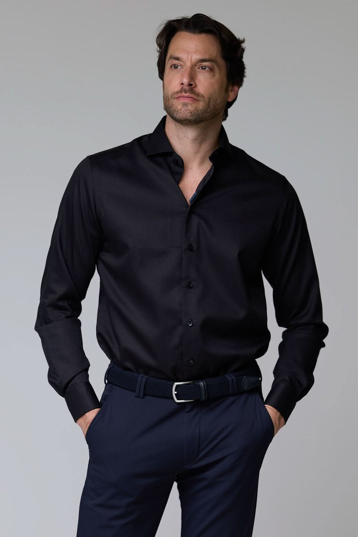 Homme portant une chemise habillée satinée noire avec manches longues et coupe ajustée, idéale pour un look professionnel.